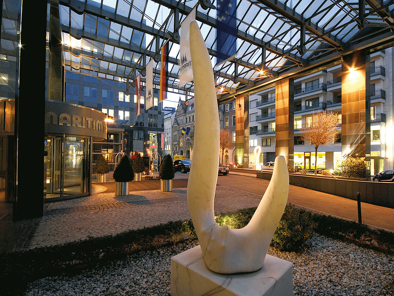 Eingang des Hotels Eingang des Maritim proArte Hotels Berlin bei Nacht, moderne Architektur mit Skulpturen und beleuchteter Glasüberdachung.
