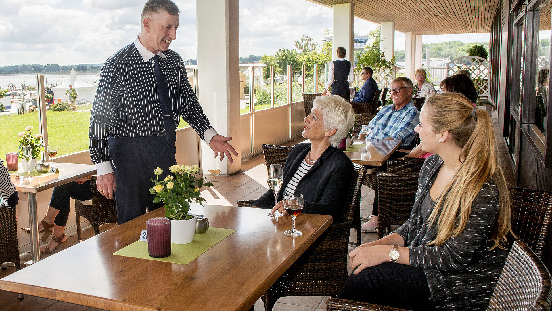 Gäste genießen Getränke und Gespräche auf der Terrasse des Maritim Hotel Travemünde mit Ostseeblick.