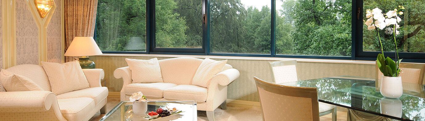 Suite  Luxuriöse Suite im Maritim Bremen mit eleganter Sitzecke, Glas-Esstisch und großem Panoramafenster mit Blick ins Grüne