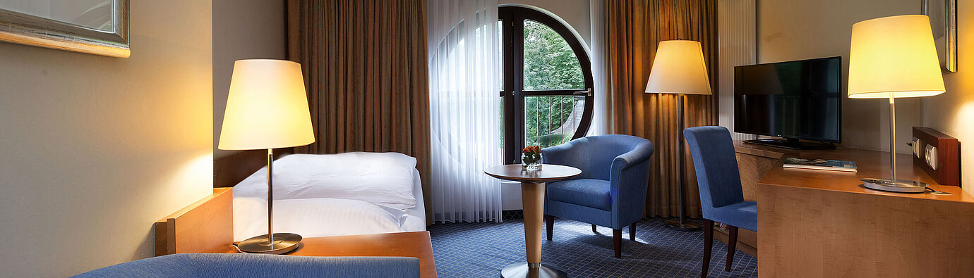 Classic Zimmer Classic Zimmer im Maritim Hotel Fulda mit Einzelbett, Schreibtisch, Sitzbereich und rundem Fenster mit Ausblick.
