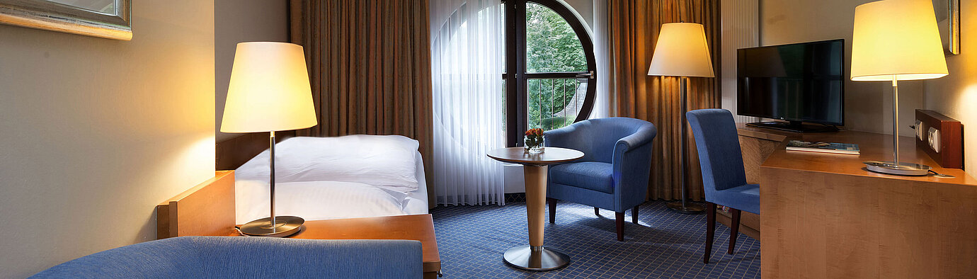 Classic Zimmer im Maritim Hotel Fulda mit Einzelbett, Schreibtisch, Sitzbereich und rundem Fenster mit Ausblick.
