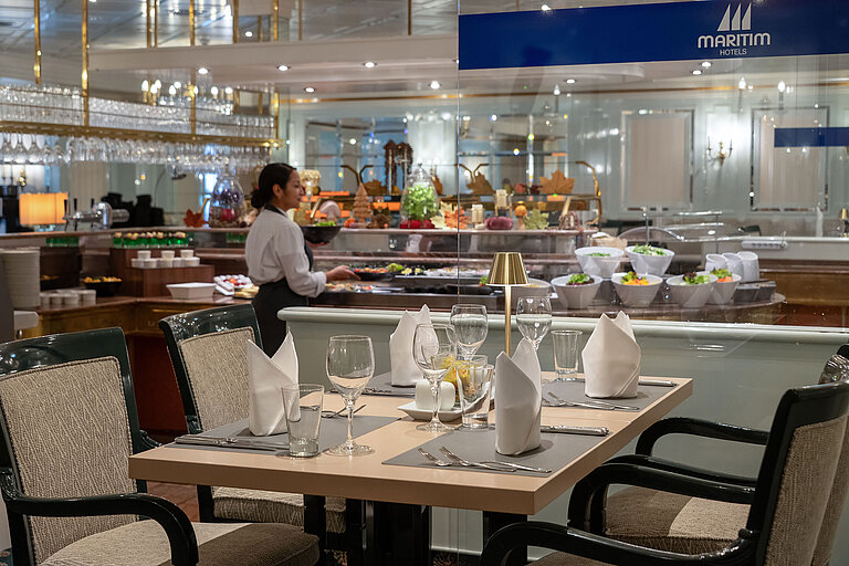 Restaurantbereich mit gedecktem Tisch, Buffetstation im Hintergrund und Servicekraft im Maritim Hotel.