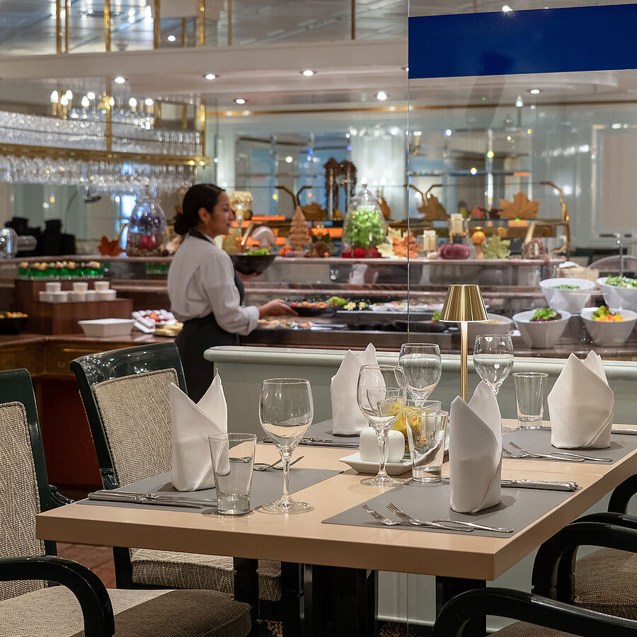 Restaurant Restaurantbereich mit gedecktem Tisch, Buffetstation im Hintergrund und Servicekraft im Maritim Hotel.