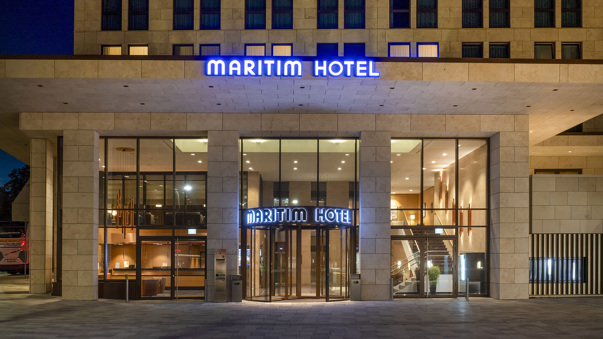 Beleuchteter Eingang des Maritim Hotel Ingolstadt mit moderner Glasfassade bei Nacht.