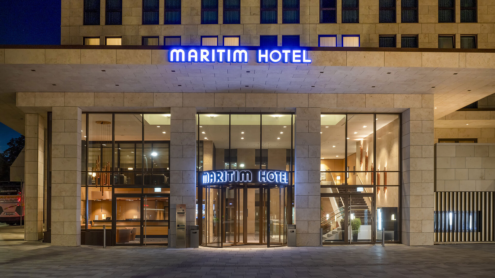 Beleuchteter Eingang des Maritim Hotel Ingolstadt mit moderner Glasfassade bei Nacht.