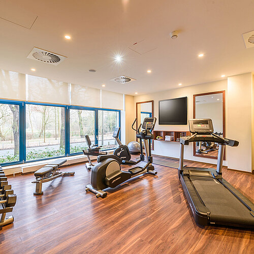 Modernes Fitnessstudio mit Ausblick im Maritim Hotel Bremen, ausgestattet mit Laufband, Hanteln und Fitnessgeräten.