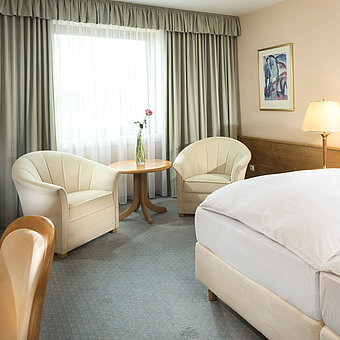 Helles Hotelzimmer mit zwei Betten, Sitzgruppe und großem Fenster im Maritim Hotel Magdeburg