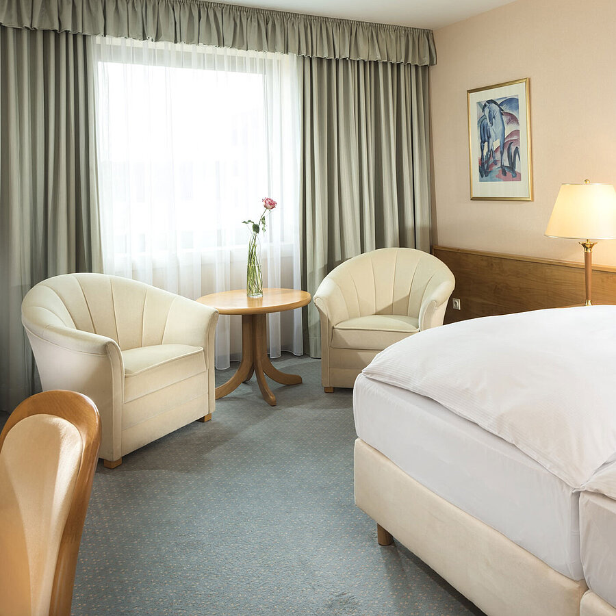 Helles Hotelzimmer mit zwei Betten, Sitzgruppe und großem Fenster im Maritim Hotel Magdeburg