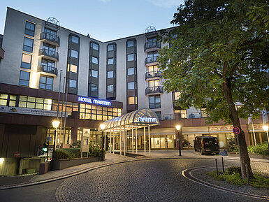 Stimmungsvoller Hoteleingang des Maritim Hotel Bad Homburg in der Abenddämmerung mit Beleuchtung.