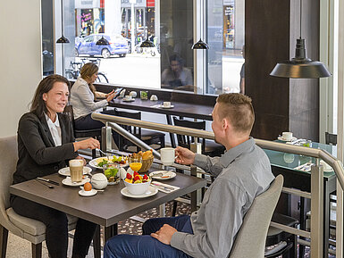 Gäste genießen ein reichhaltiges Frühstück im Maritim proArte Berlin, umgeben von moderner Atmosphäre und großen Fenstern.
