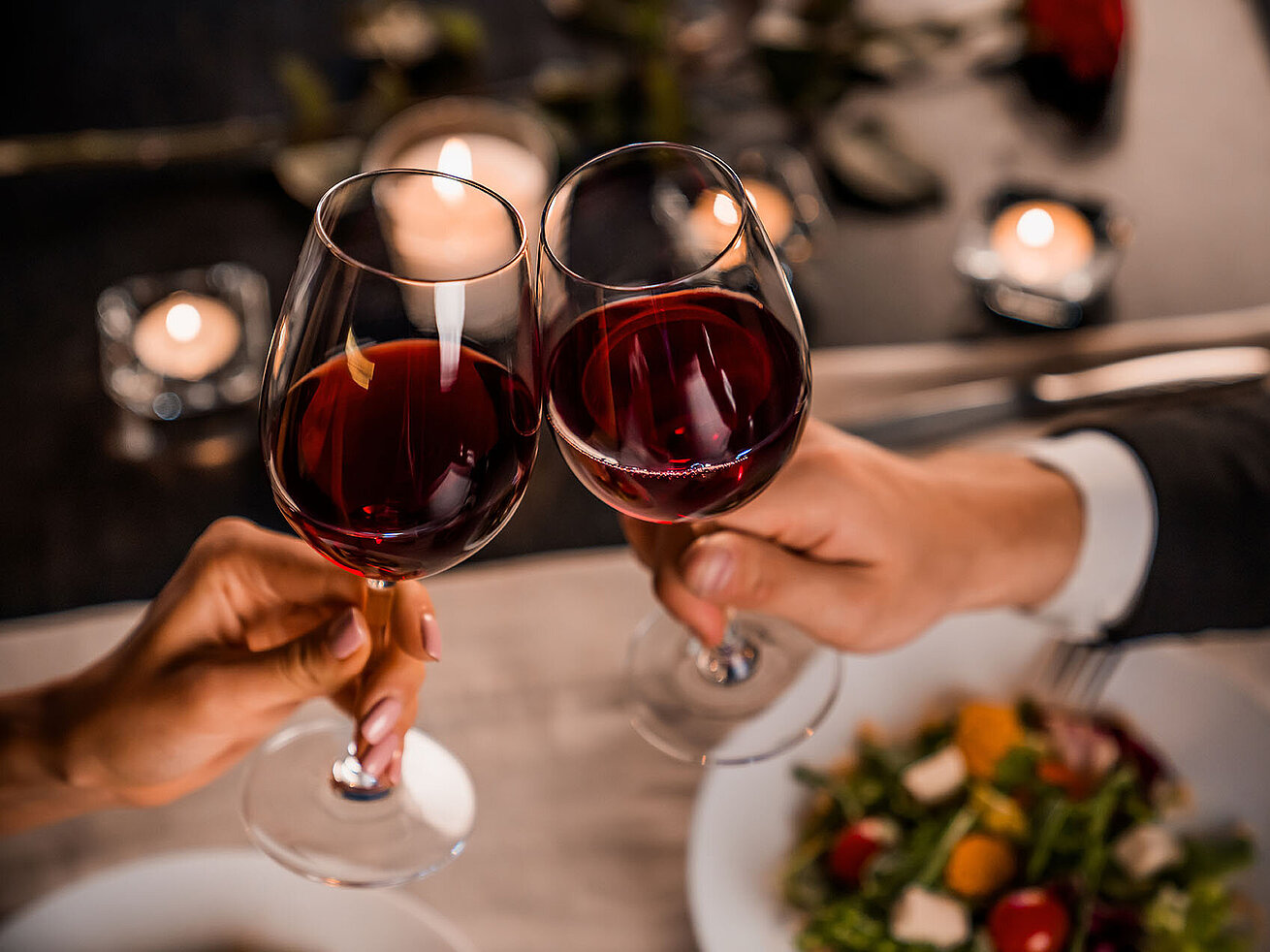 Zwei Gläser Rotwein stoßen bei einem romantischen Dinner an