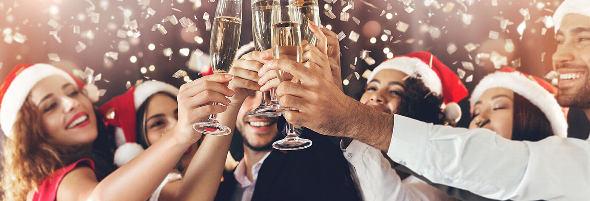 © Prostock-studio - AdobeStock.com Menschen stoßen bei einer festlichen Weihnachtsfeier mit Sekt an – fröhliche Stimmung in weihnachtlichem Ambiente
