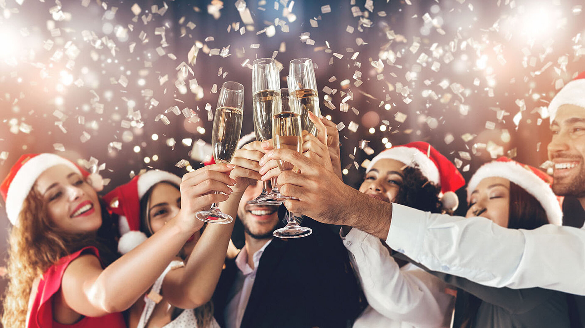 © Prostock-studio - AdobeStock.com Menschen stoßen bei einer festlichen Weihnachtsfeier mit Sekt an – fröhliche Stimmung in weihnachtlichem Ambiente