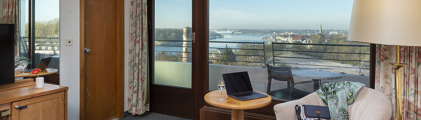 Helles Hotelzimmer mit Balkon, Schreibtisch und Ausblick auf die Trave und die Lübecker Bucht