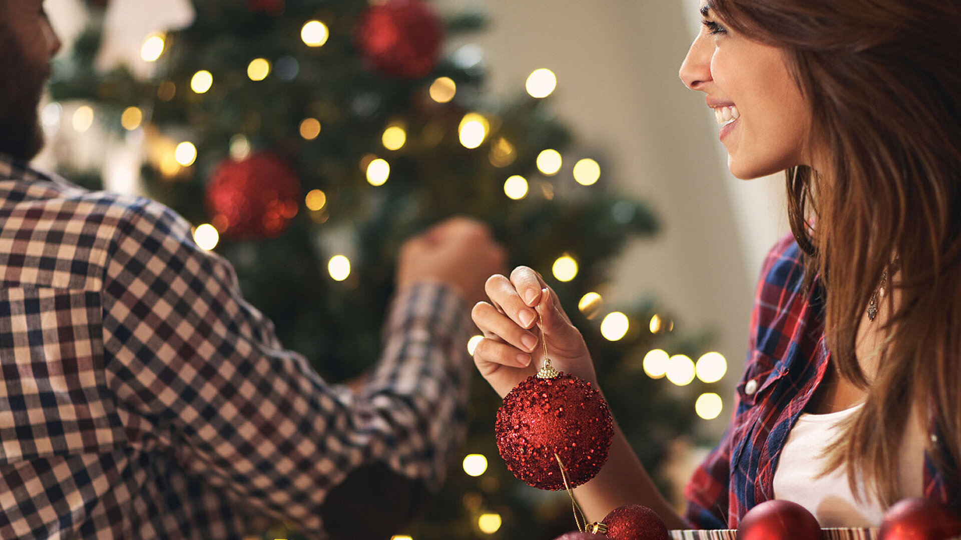 Frau schmückt Weihnachtsbaum mit roten Kugeln und Lichtern
