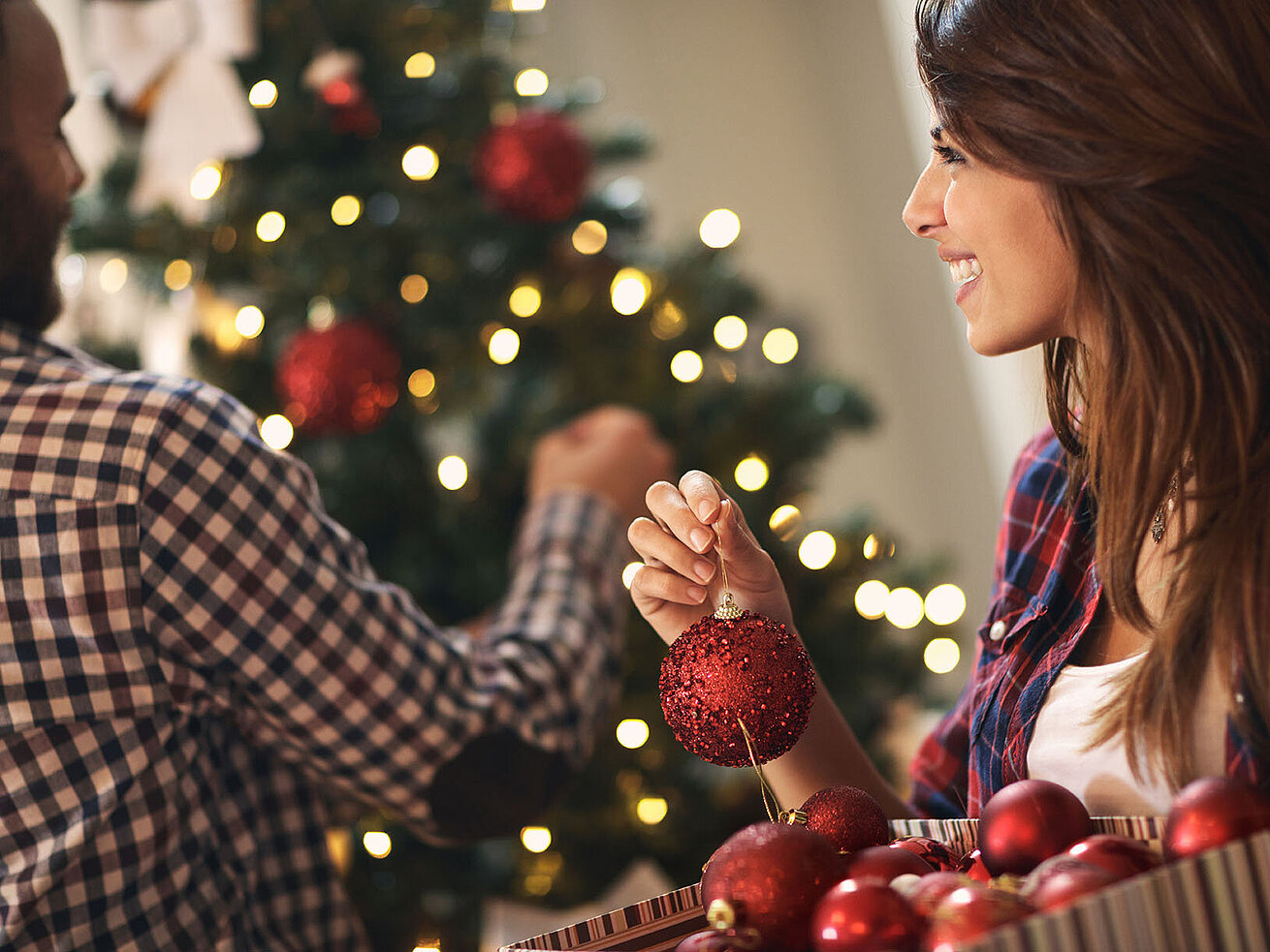 Frau schmückt Weihnachtsbaum mit roten Kugeln und Lichtern