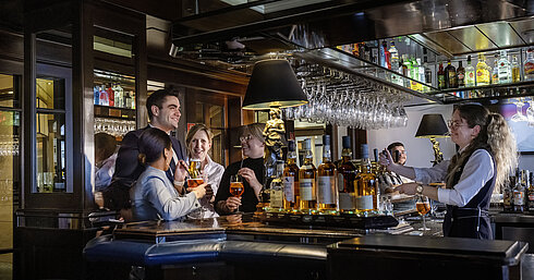Gäste genießen Cocktails und gute Stimmung in der Bar des Maritim Hotels Darmstadt. Freundliches Barpersonal serviert Drinks.