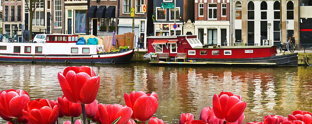 Rote und gelbe Tulpen vor Amsterdamer Grachtenhäusern mit Booten auf dem Wasser