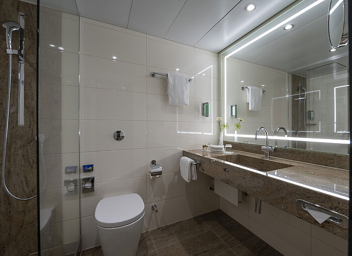 Comfort Bad Modernes Badezimmer im Maritim Hotel Bremen mit luxuriösen Armaturen, großem Spiegel mit Beleuchtung und ebenerdiger Dusche.