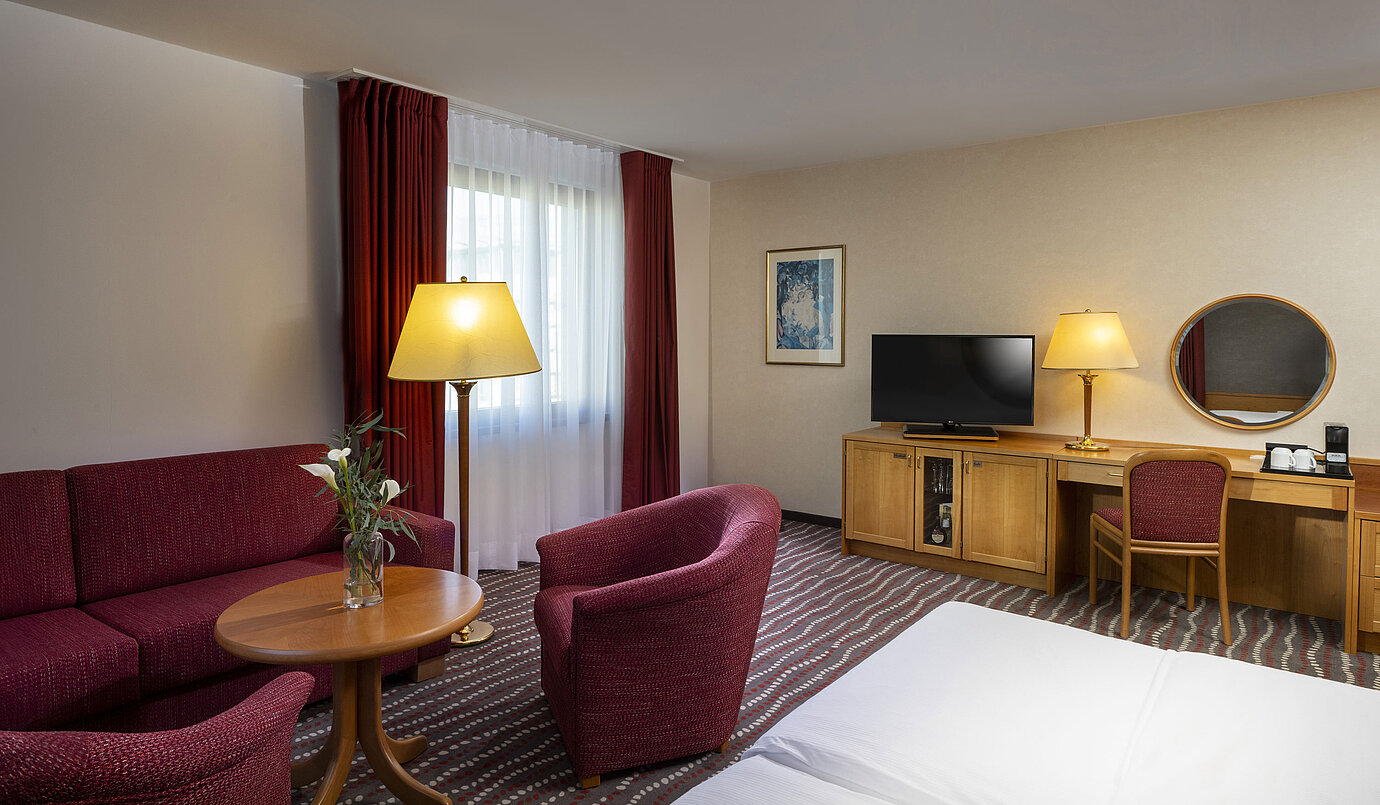 Komfortables Studiozimmer im Maritim Hotel Magdeburg mit Sitzecke, Schreibtisch und modernem TV.