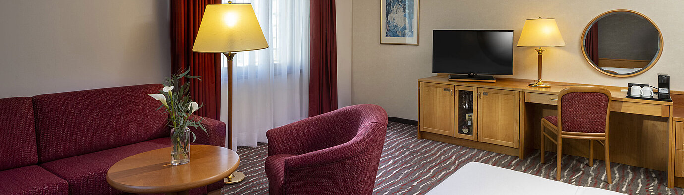 Komfortables Studiozimmer im Maritim Hotel Magdeburg mit Sitzecke, Schreibtisch und modernem TV.
