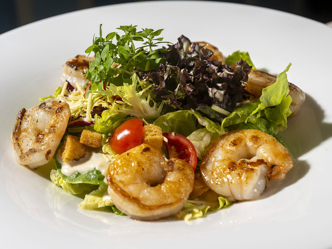 Gebratene Garnelen auf frischem Blattsalat mit Kirschtomaten und mediterranen Beilagen.