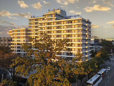 Außenansicht des Maritim Hotel Darmstadt bei Sonnenuntergang mit moderner Architektur und Bäumen im Vordergrund.