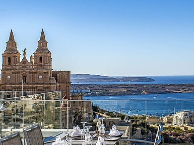 Rooftop-Restaurant mit gedeckten Tischen, Blick auf Kirche, Küste und blaues Mittelmeer