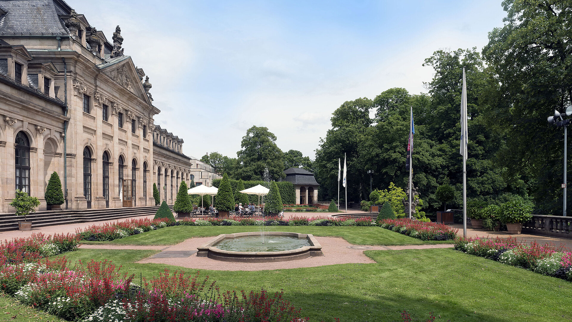 Außenansicht Die barocke Orangerie Fulda mit blühendem Garten, Terrasse und historischem Pavillon im Hintergrund.
