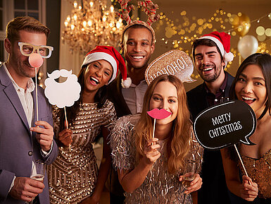 Elegante Gruppe bei festlicher Weihnachtsfeier mit Sekt und Weihnachtsmützen vor goldenem Hintergrund