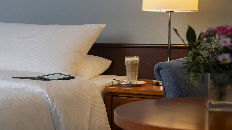 Detailaufnahme eines gemütlichen Classic-Zimmers mit Bett, Nachttisch, Latte Macchiato und moderner Beleuchtung.