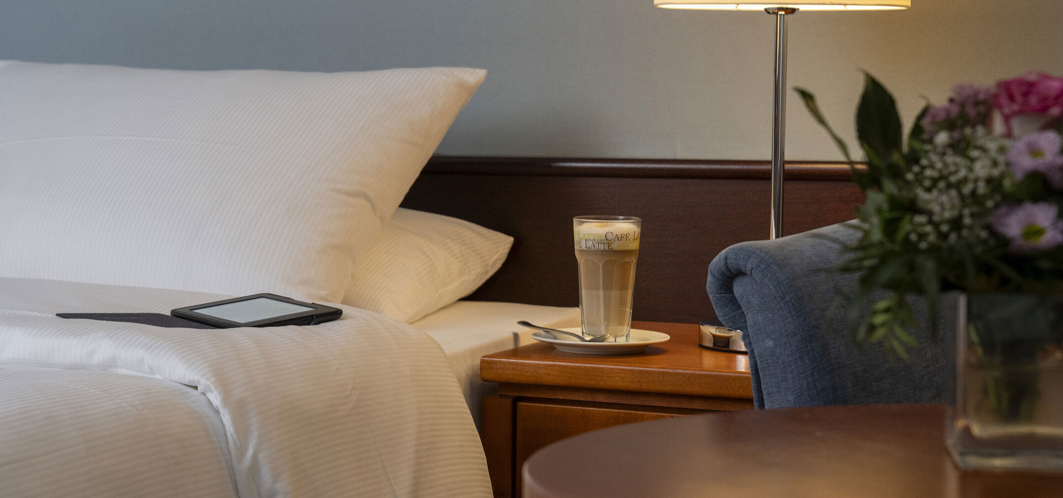 Detailaufnahme eines gemütlichen Classic-Zimmers mit Bett, Nachttisch, Latte Macchiato und moderner Beleuchtung.