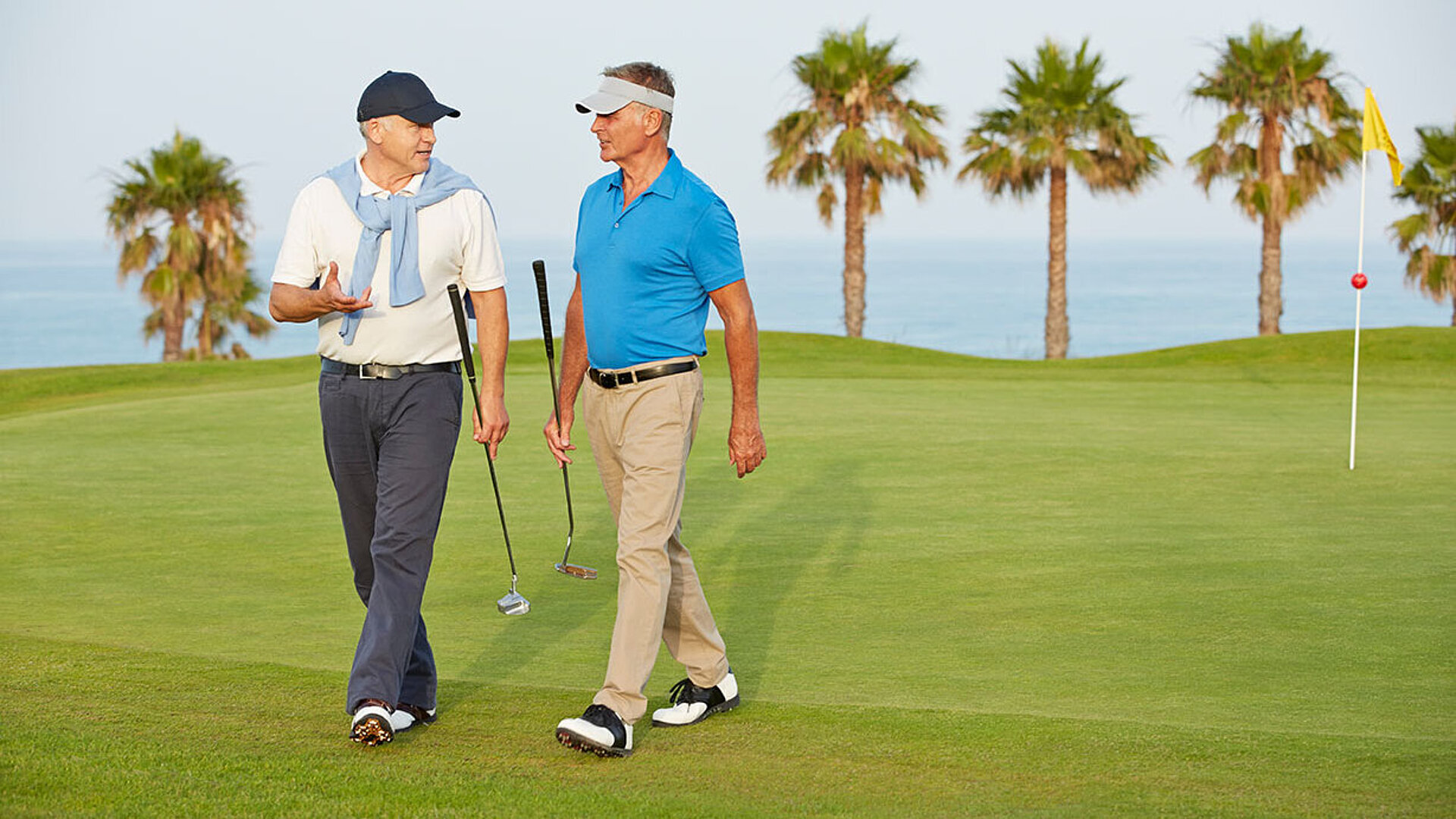 © Chris RyanKOTO - AdobeStock.com Zwei Golfer gehen über den Golfplatz und unterhalten sich zwischen den Spielbahnen.