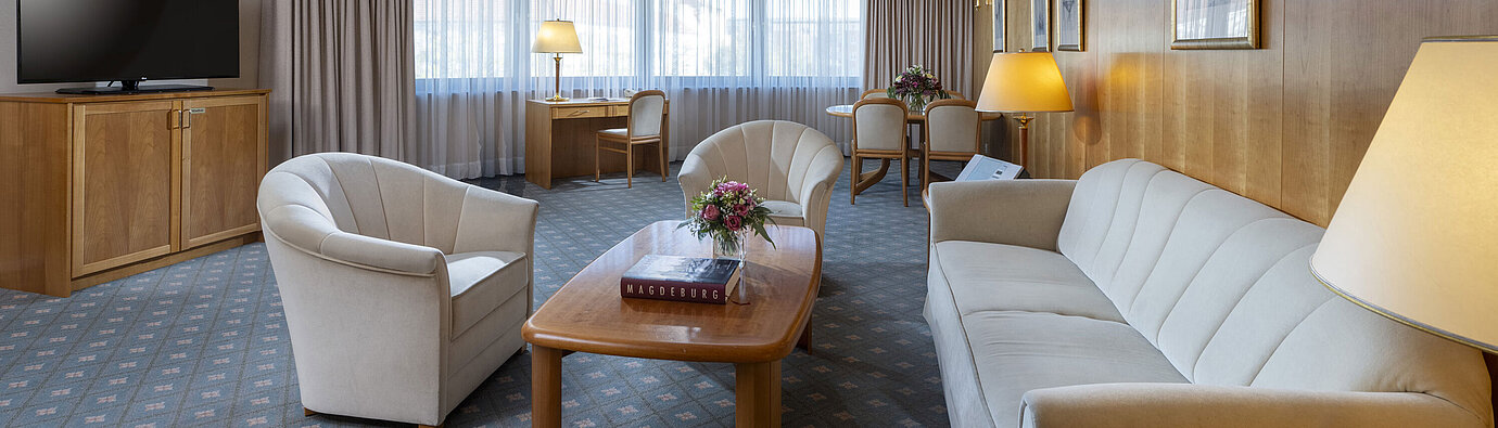 Großzügiges Wohnzimmer einer Suite im Maritim Hotel Magdeburg mit eleganter Einrichtung, Sitzecke und Arbeitsplatz.