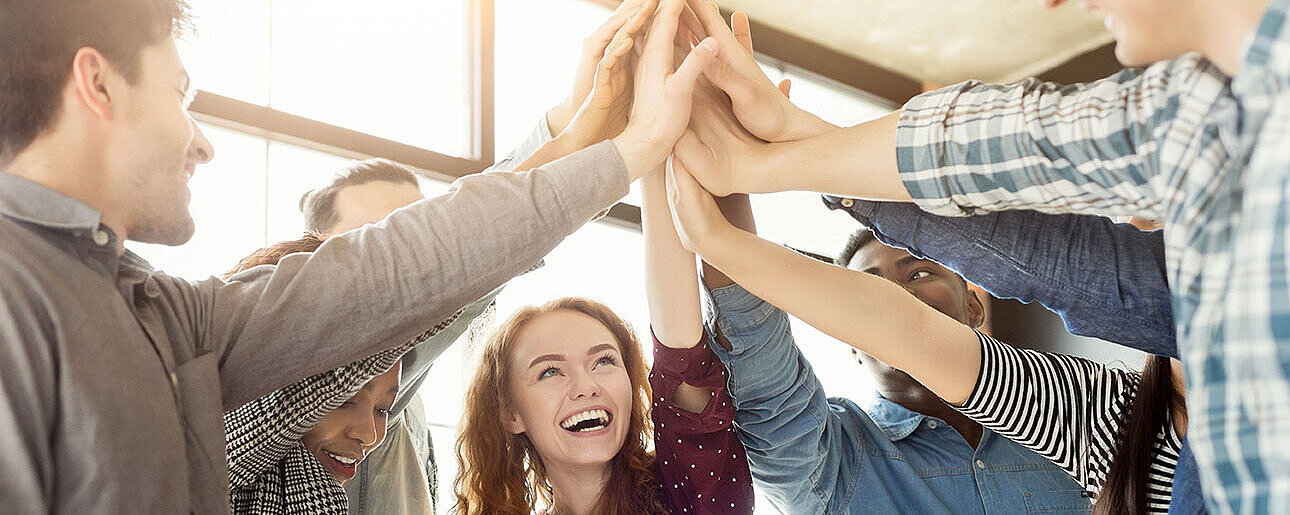 Gruppe von jungen Menschen gibt sich ein High-Five und feiert gemeinsam einen Erfolg.