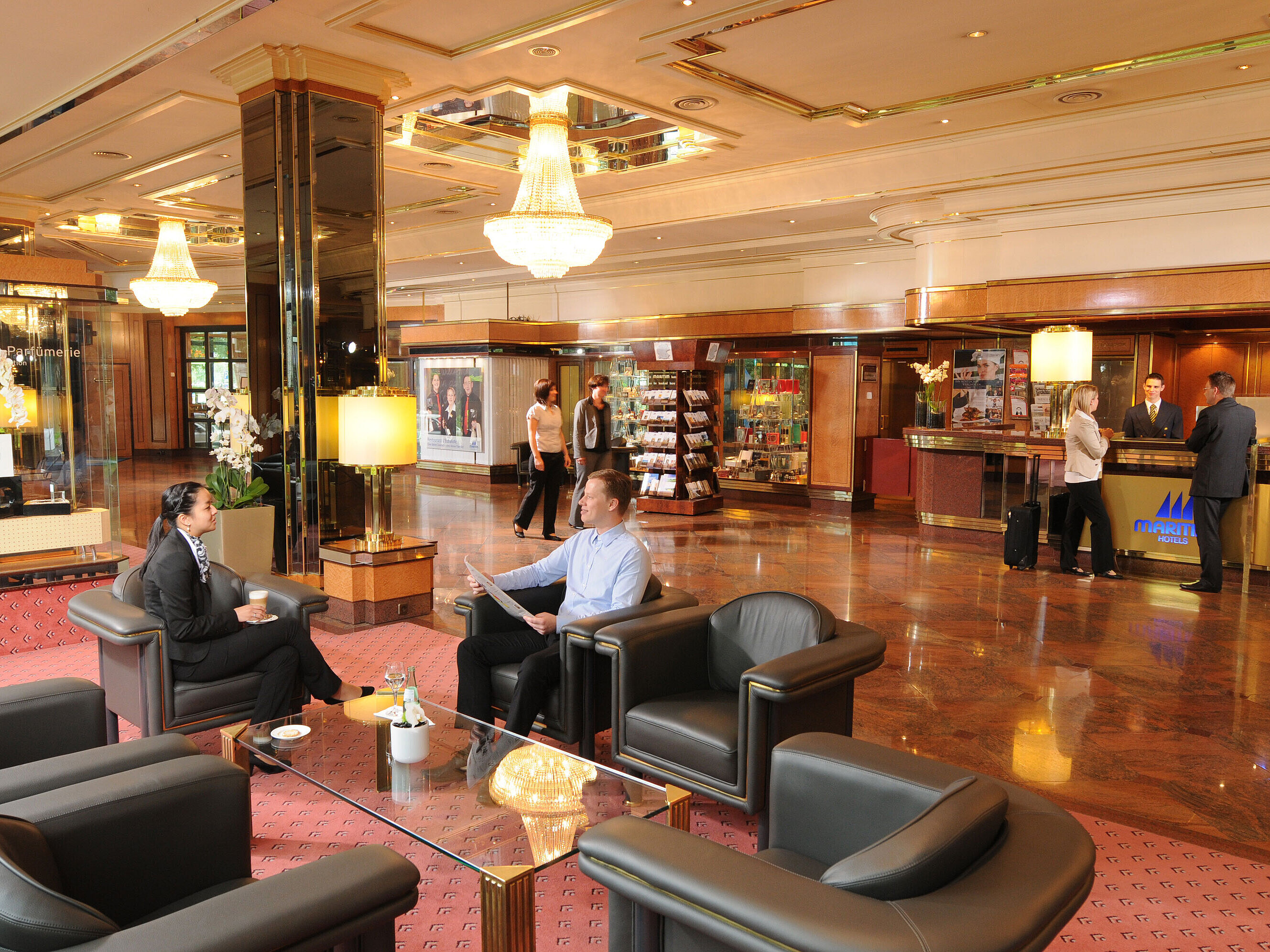 Geräumige Lobby im Maritim Bremen mit eleganten Sitzgelegenheiten,Gästen im Gespräch und Empfangspersonal am Check-in-Bereich