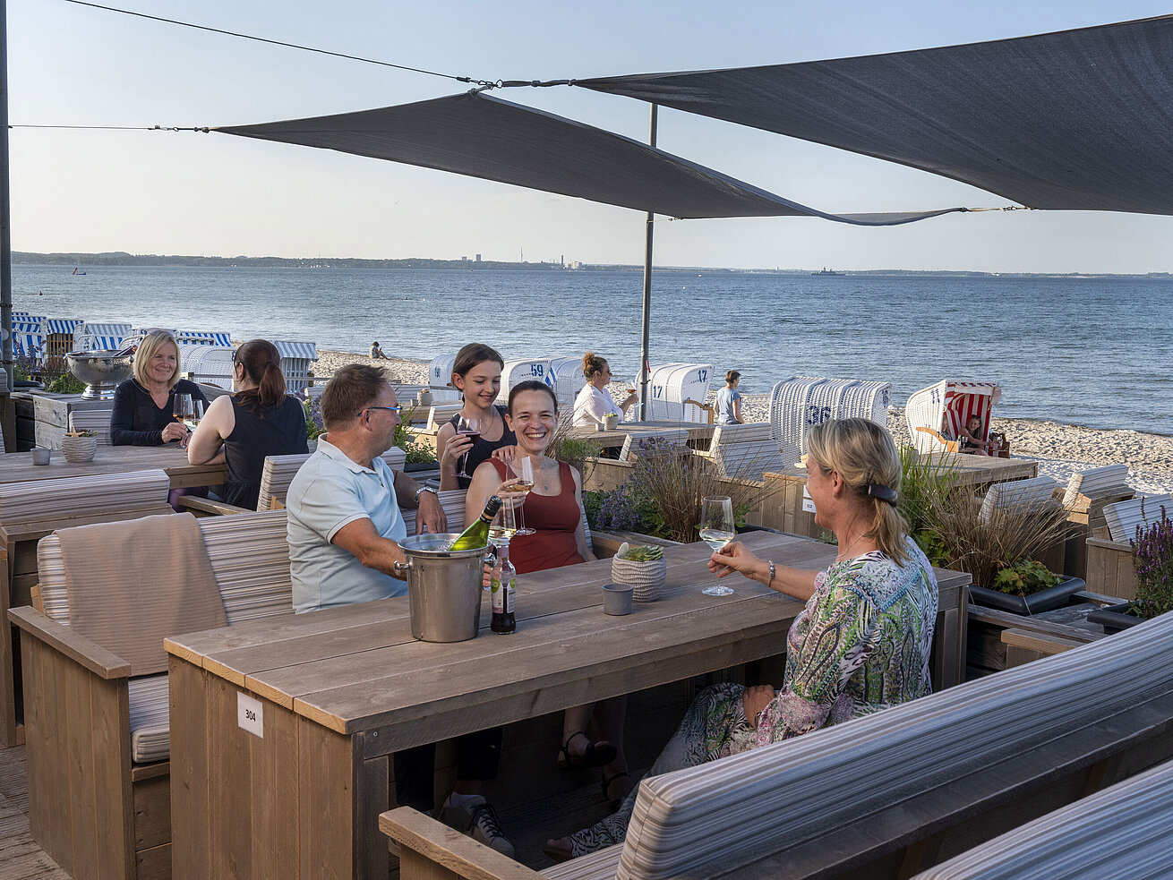 Gruppe von Gästen in der Strandbar des Maritim Seehotel Timmendorfer Strand, genießt Drinks mit Meerblick und Strandkörben.