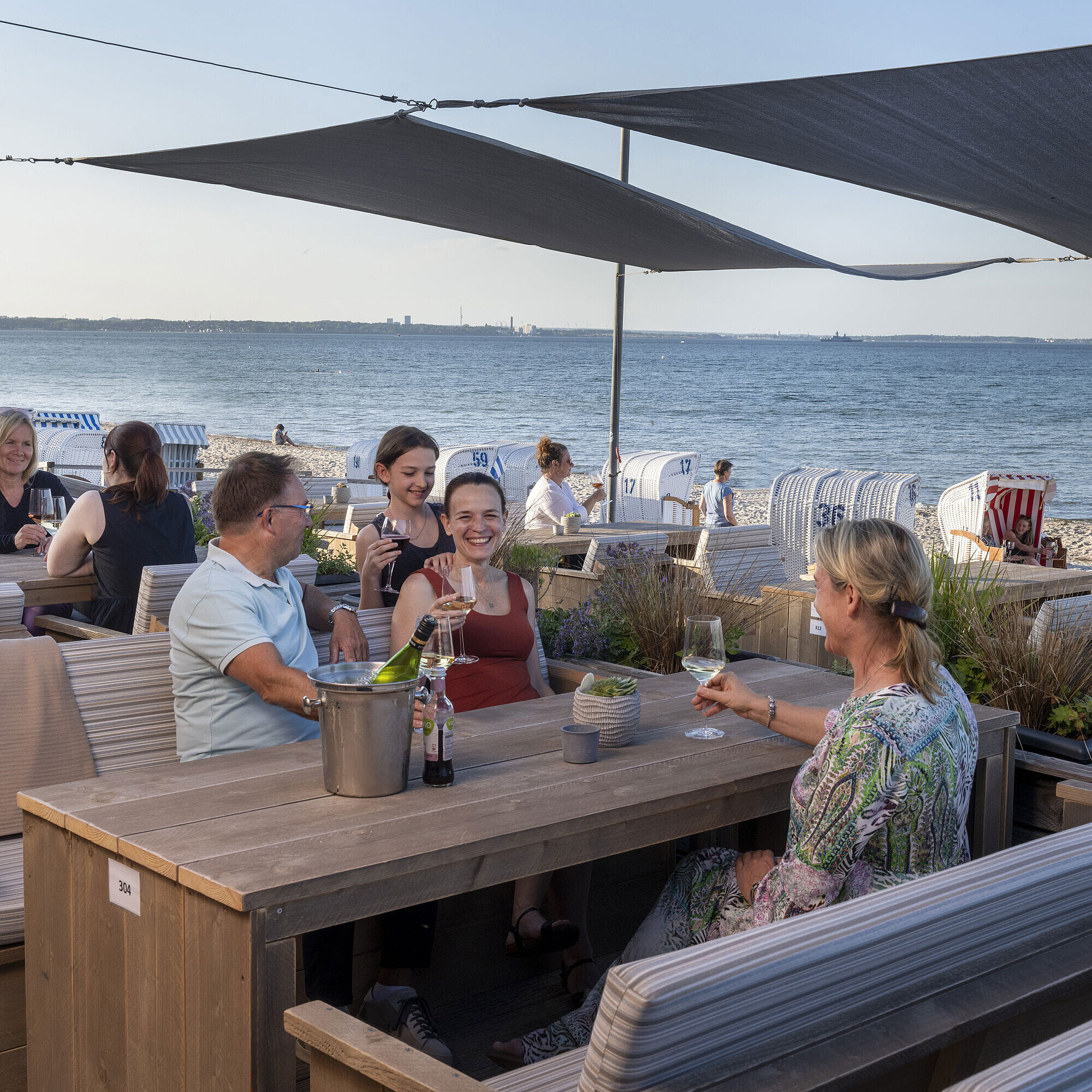 Gruppe von Gästen in der Strandbar des Maritim Seehotel Timmendorfer Strand, genießt Drinks mit Meerblick und Strandkörben.