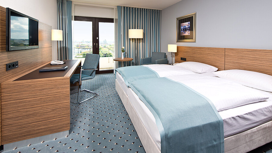 Comfort Zimmer im Maritim Hotel Darmstadt mit modernem Design, Schreibtisch, Sitzbereich und Blick auf große Fenster.