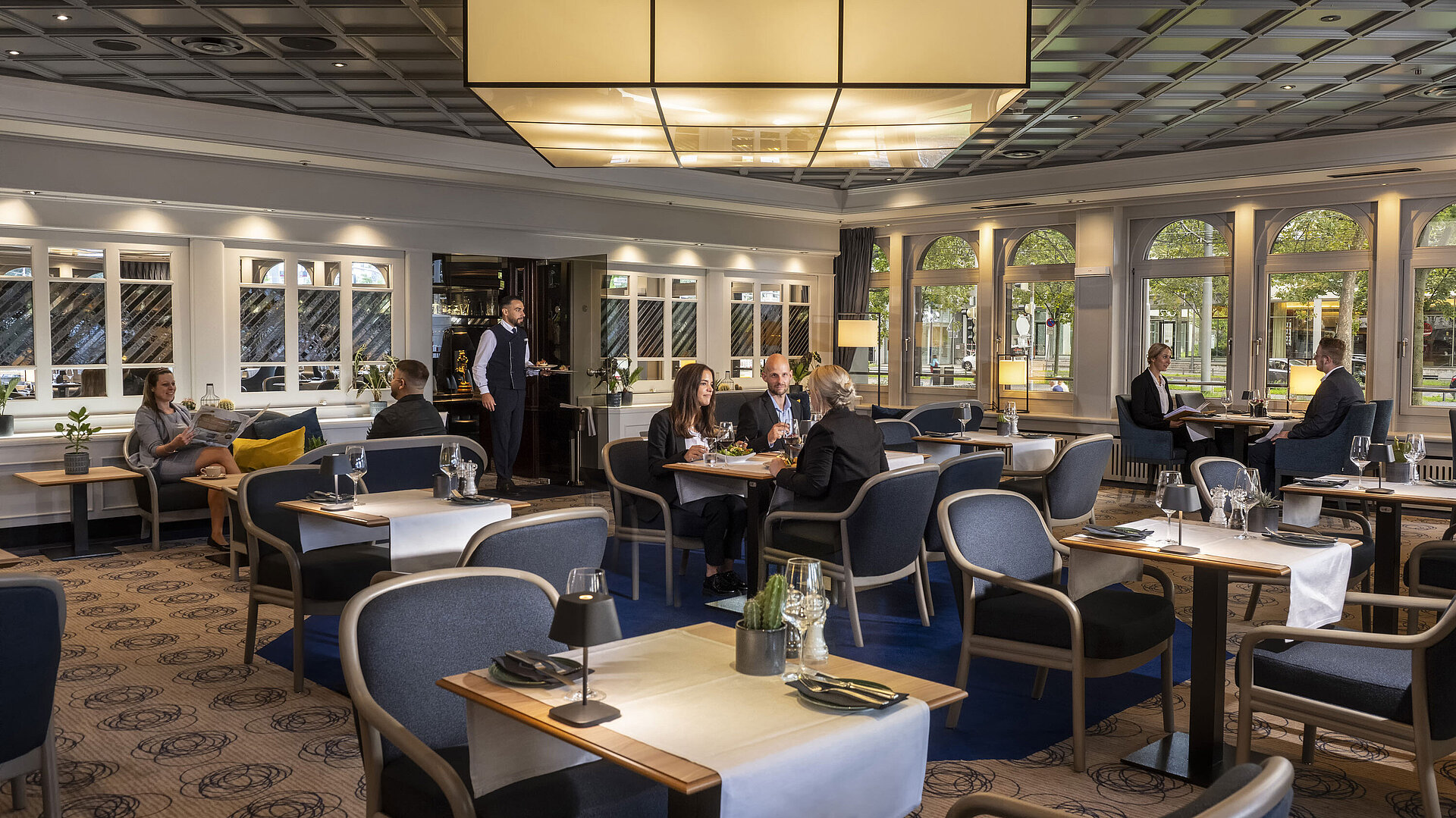 Elegantes Restaurant mit Gästen, die speisen und entspannen. Moderne Einrichtung und große Fenster mit Ausblick.