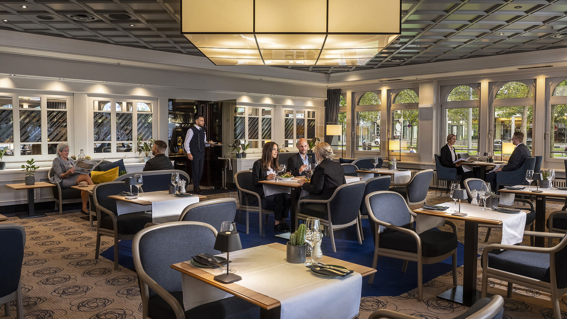 Elegantes Restaurant mit Gästen, die speisen und entspannen. Moderne Einrichtung und große Fenster mit Ausblick.