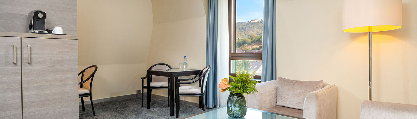 Wohnbereich der Junior Suite im Maritim Hotel Königswinter mit Sitzgruppe, Couchtisch und Fenster.