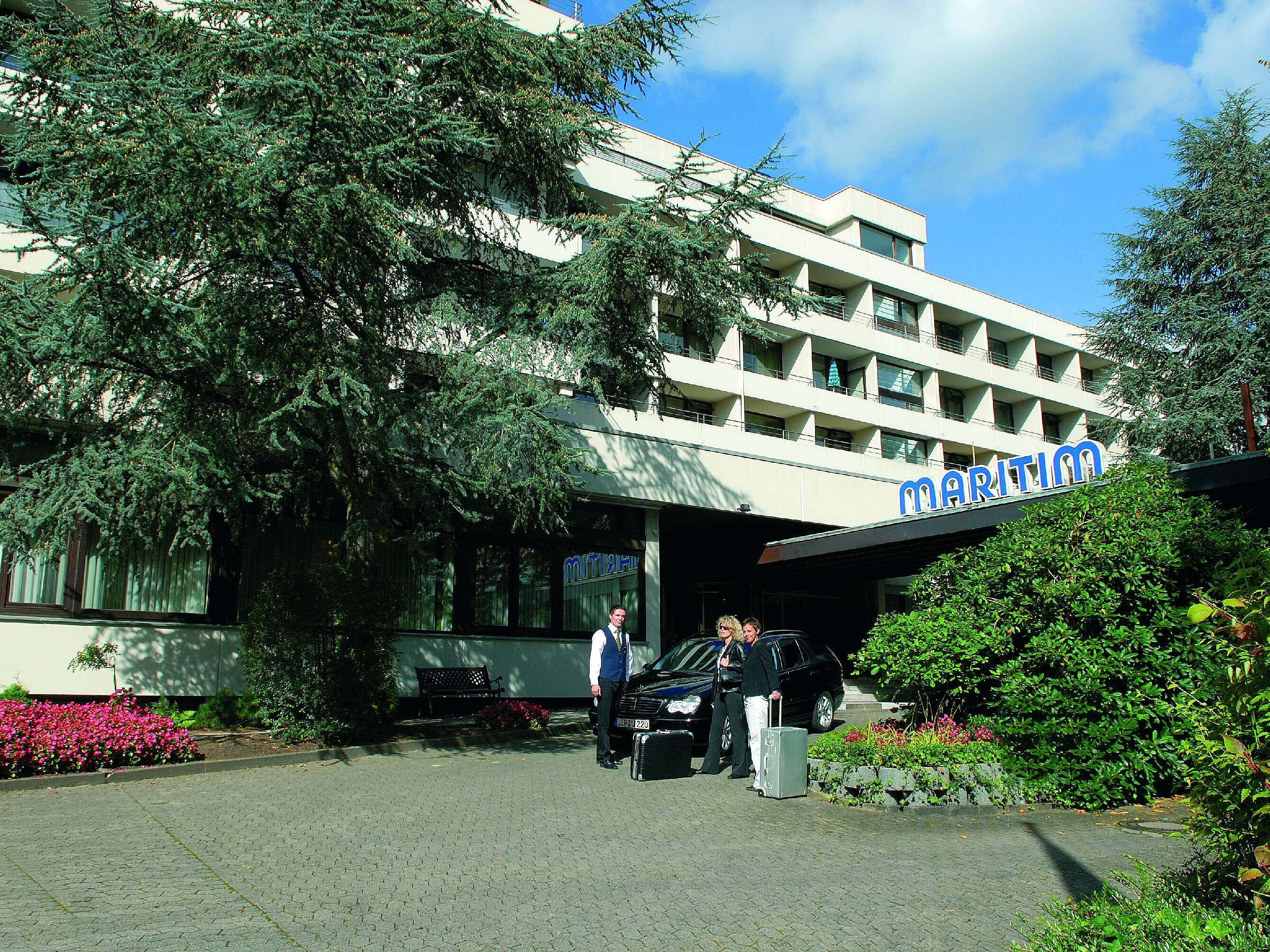 Gäste treffen am Eingang des Maritim Hotel Bad Salzuflen ein, umgeben von Bäumen und gepflegtem Grün