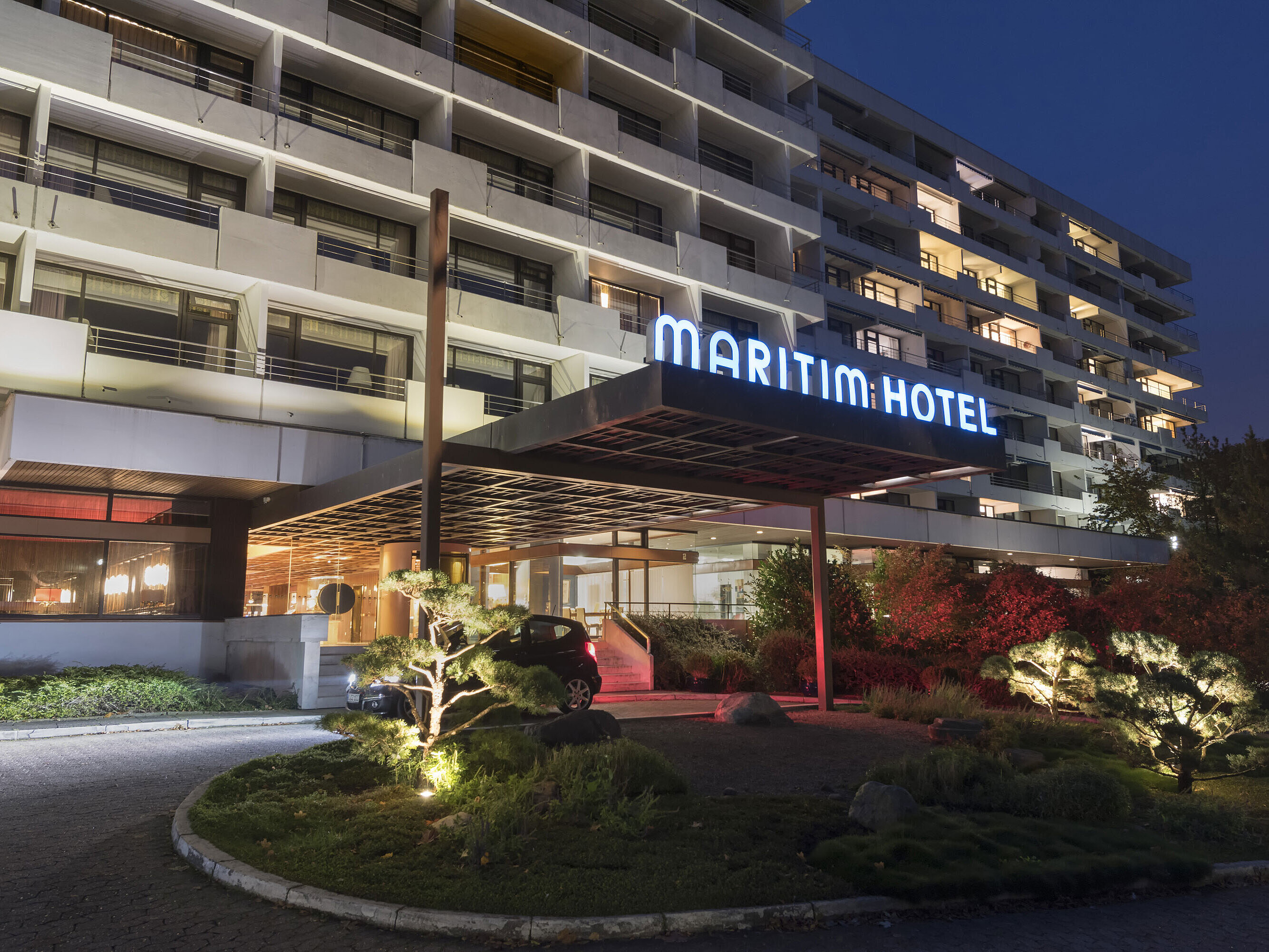 Außenansicht des Maritim Hotel Kiel bei Nacht, beleuchteter Hoteleingang und moderne Architektur mit Balkonen und gepflegtem Garten.