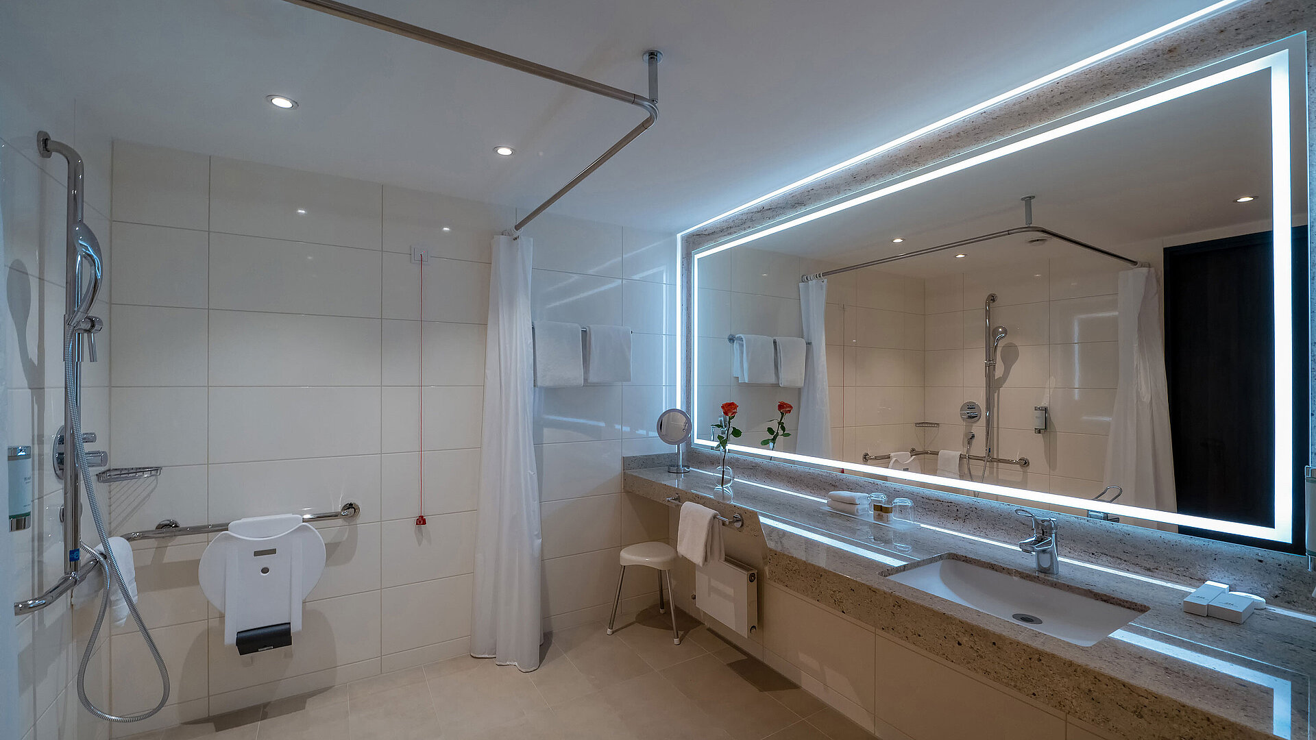 Modernes Badezimmer der Junior Suite mit Doppelwaschbecken, großer Spiegelwand, Dusche und eleganter Beleuchtung.