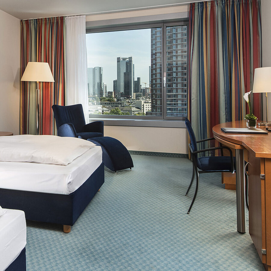 Comfort Zimmer im Maritim Hotel Frankfurt mit zwei Einzelbetten, Schreibtisch, Sitzbereich und Blick auf die Skyline.