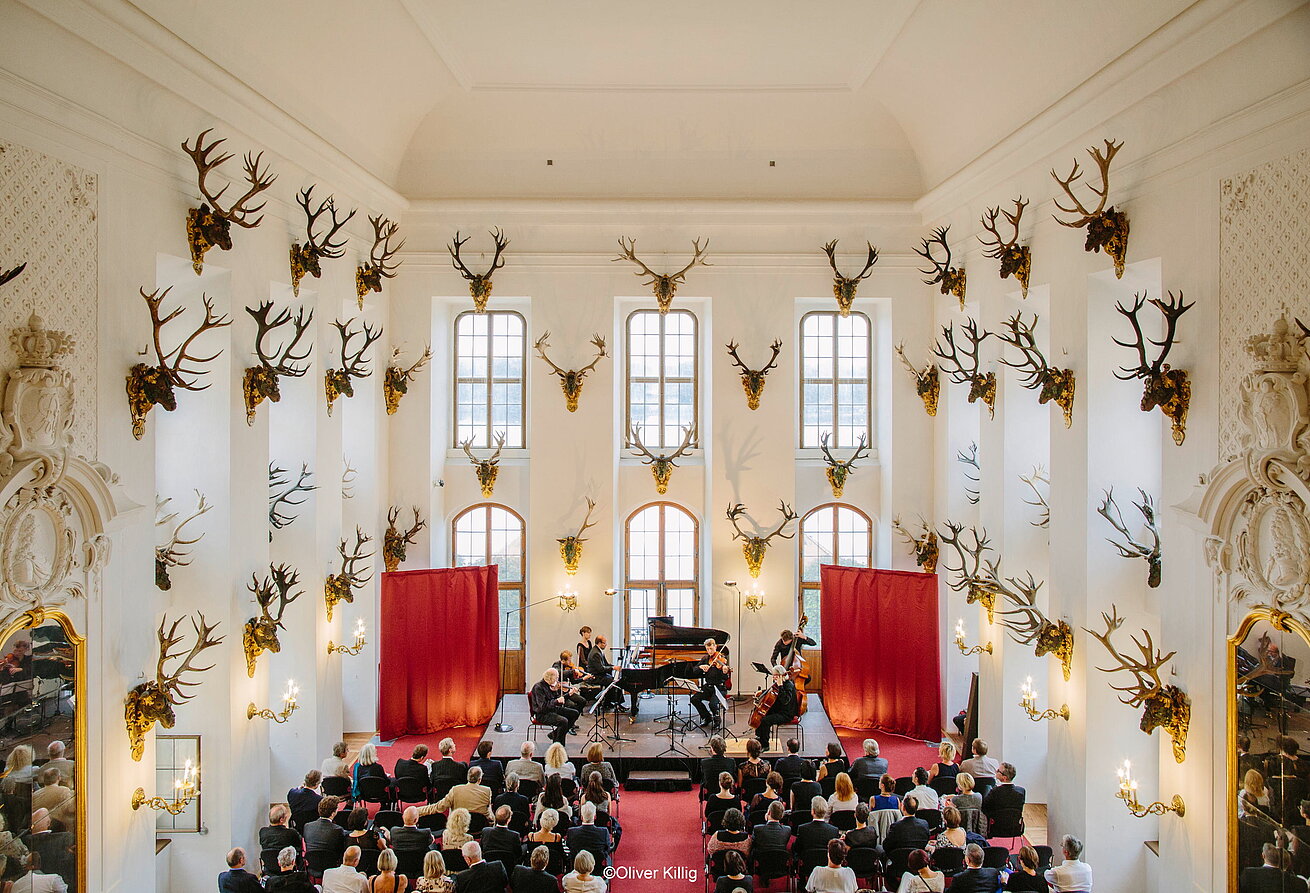 Konzert im historischen Saal mit Hirschgeweihen, Bühne und Publikum