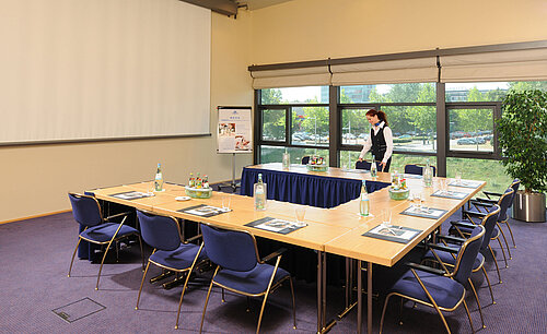 Tagungsraum im Maritim Hotel Dresden mit U-förmiger Tischanordnung, Präsentationsleinwand und Vorbereitungen für ein Meeting.