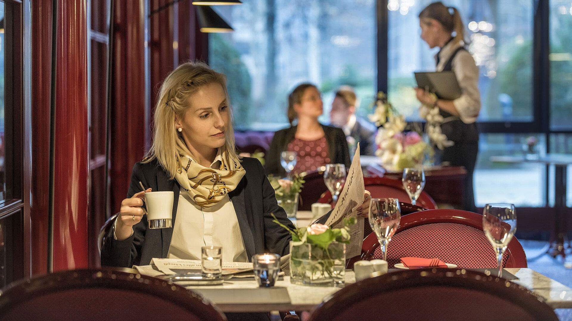 Frau genießt Kaffee im Café "Brasserie" des Maritim Hotel Bonn mit roter Einrichtung und entspannter Atmosphäre.