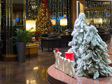 Festlich dekorierte Hotellobby mit geschmückten Weihnachtsbäumen, Kronleuchter und winterlicher Atmosphäre.